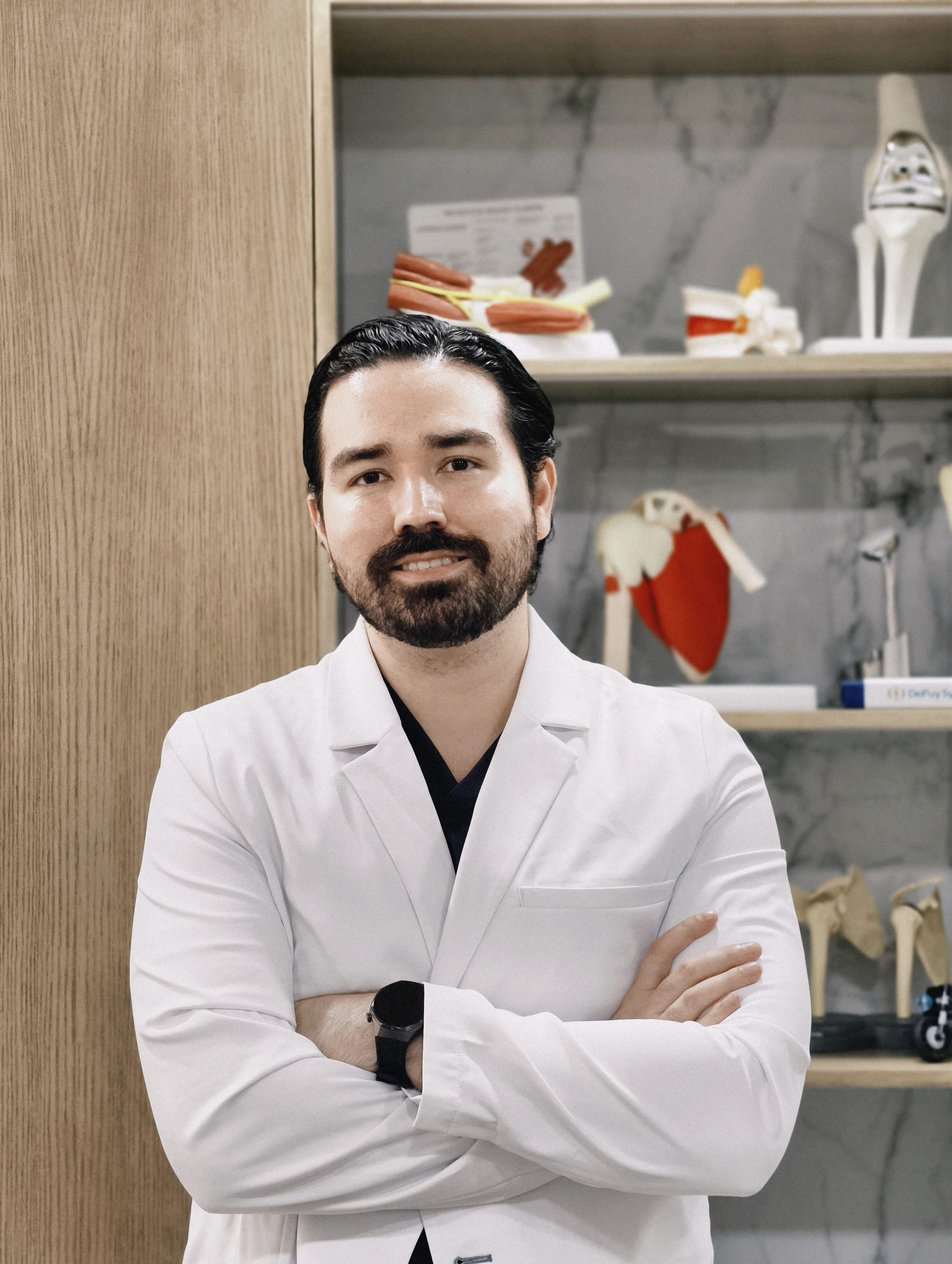 Dr. Braulio Ayala, traumatólogo en Monterrey, junto a modelos anatómicos de rodilla y hombro en su consultorio