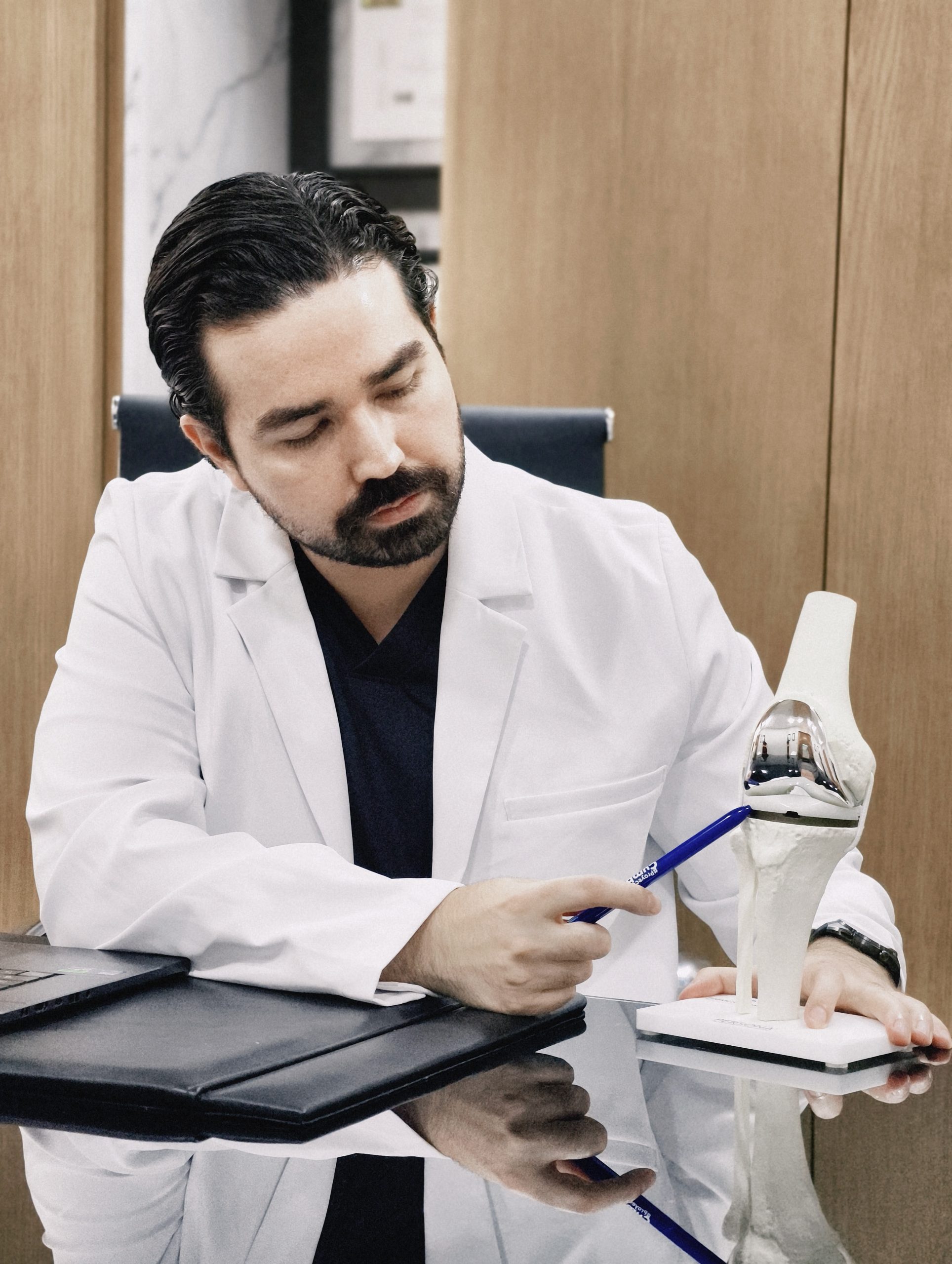 Dr. Braulio Ayala señalando un modelo de prótesis de rodilla sobre su escritorio en Monterrey