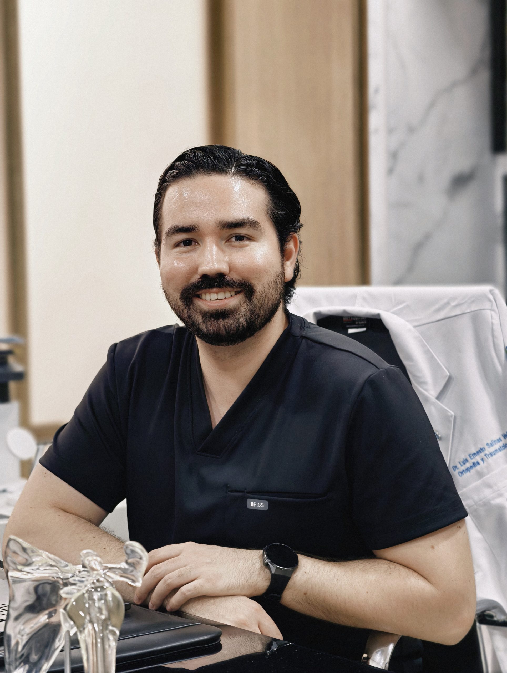 Dr. Braulio Ayala sonriendo en su consultorio, con un modelo anatómico de hombro sobre el escritorio
